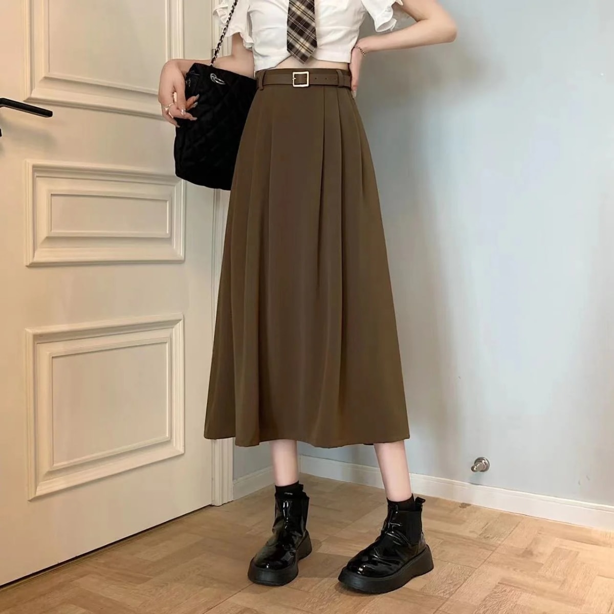Model wearing high-waisted pleated A-line midi skirt with belt.