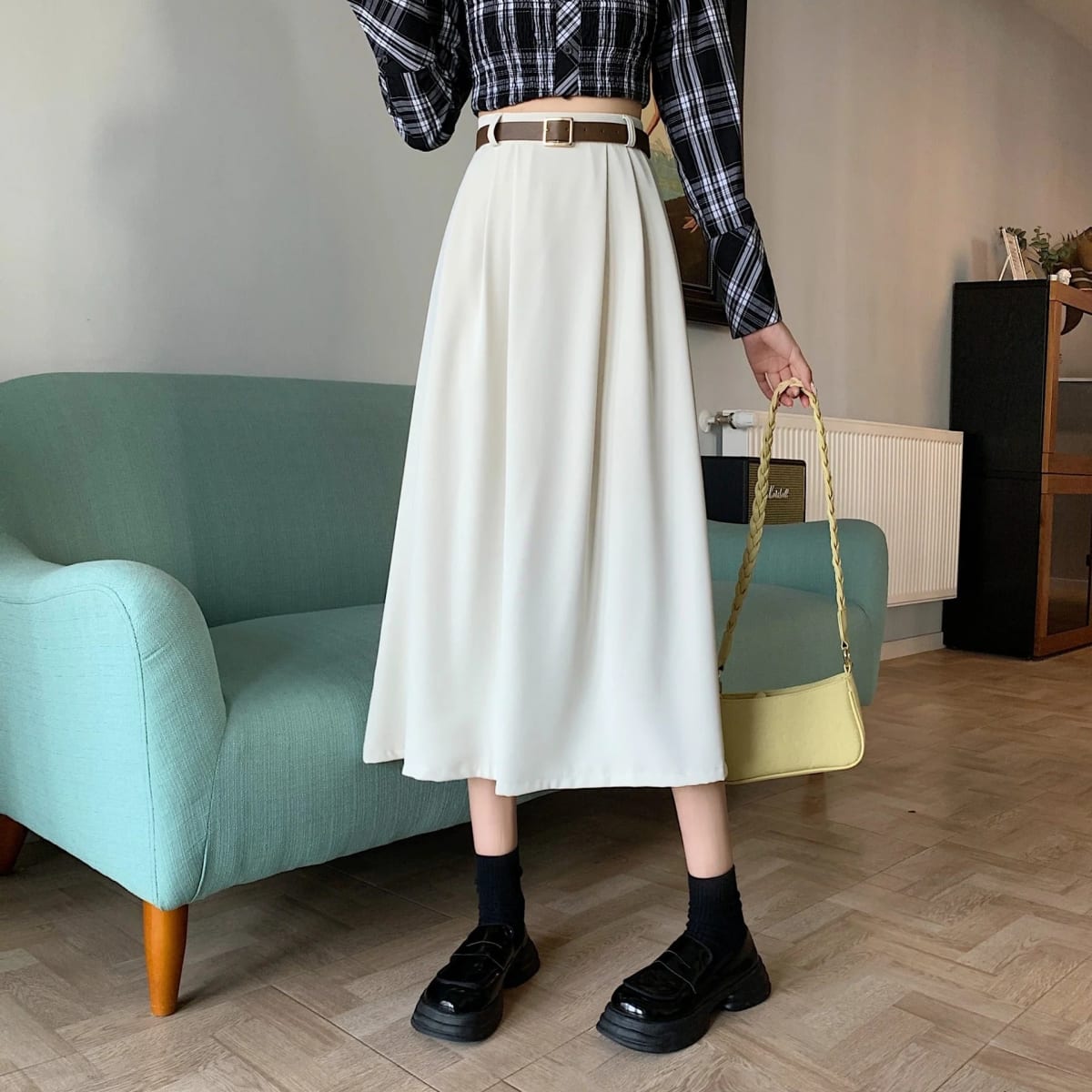 Model wearing high-waisted pleated A-line midi skirt with belt.