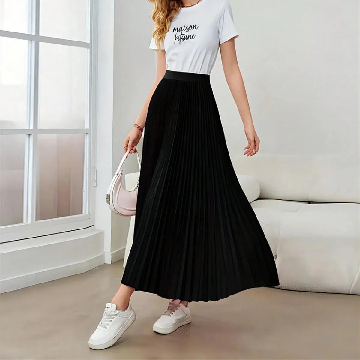 Model wearing a high-waisted pleated midi skirt with a white top and sneakers.