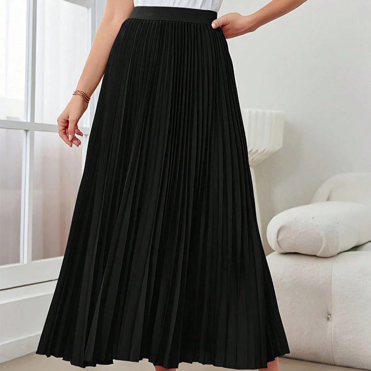 Model wearing a high-waisted pleated midi skirt with a white top and sneakers.