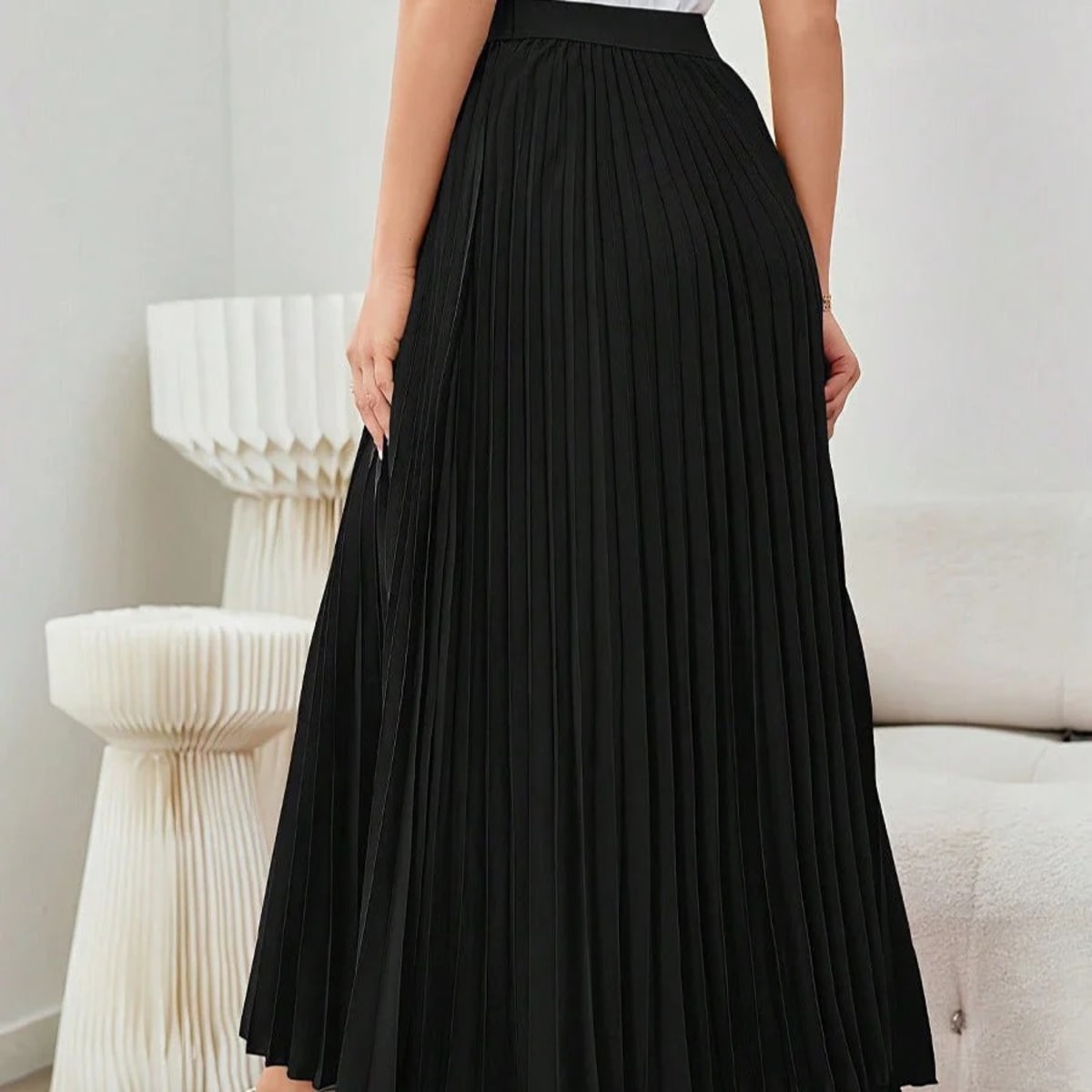 Model wearing a high-waisted pleated midi skirt with a white top and sneakers.