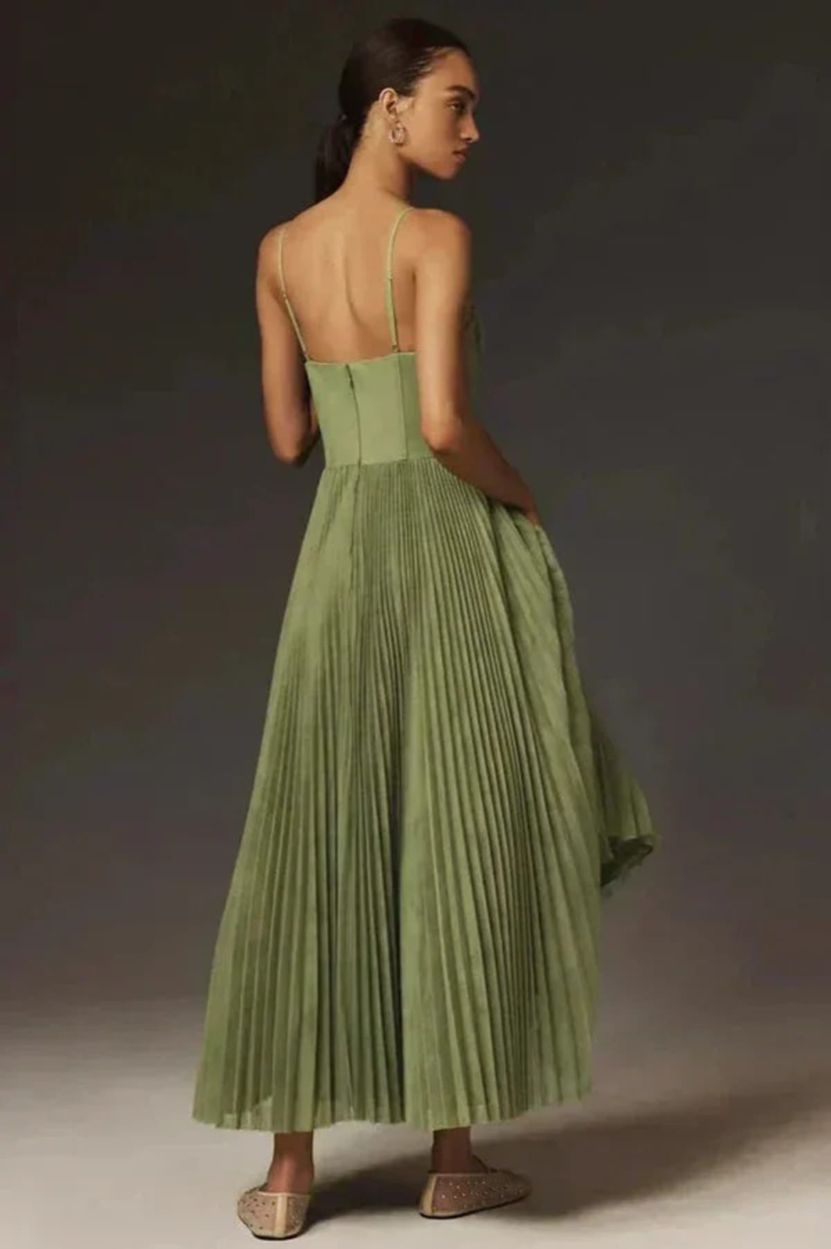 Woman wearing a sage green bustier midi dress with pleats.