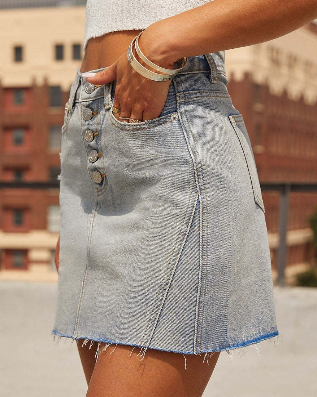 Woman wearing a denim mini skirt with button-front and raw hem.