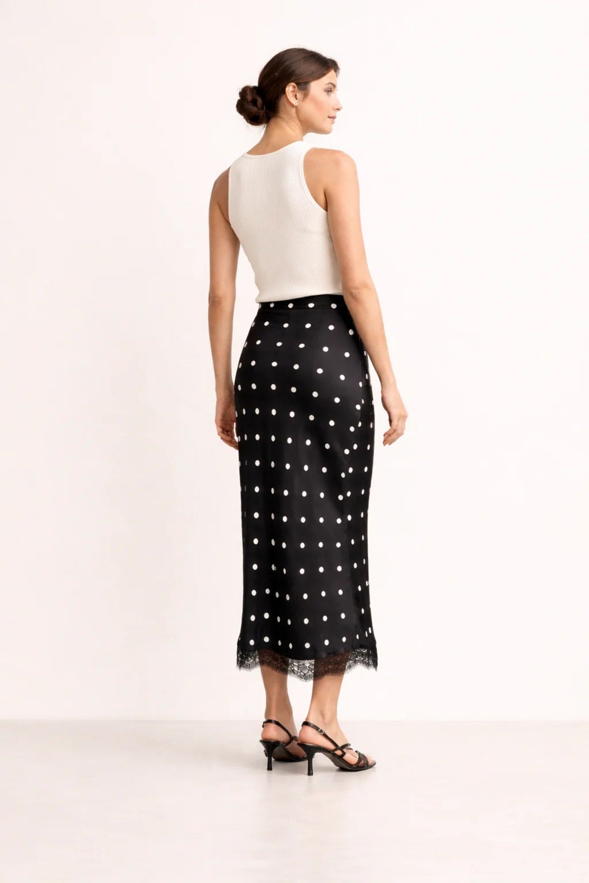 Woman wearing a midi slip skirt with polka dots and lace trim.