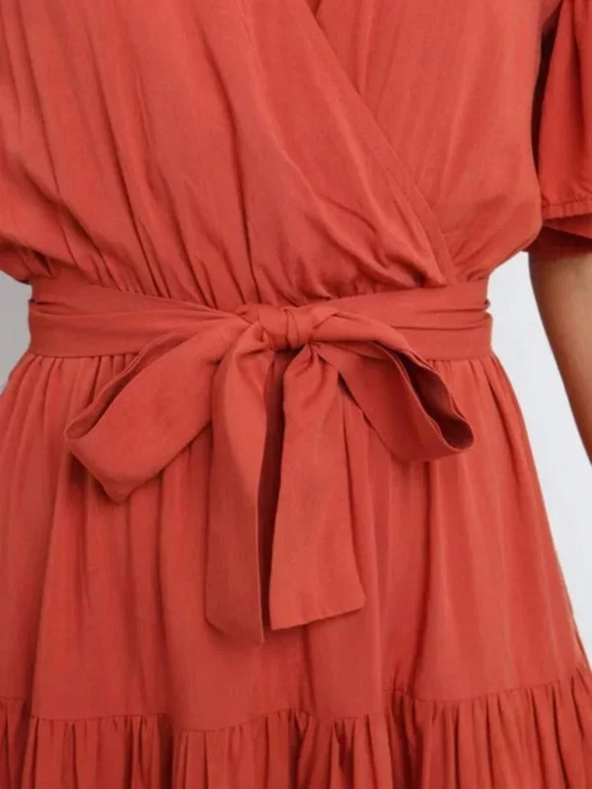 Woman in rust-colored midi dress with V-neck and tie waist.