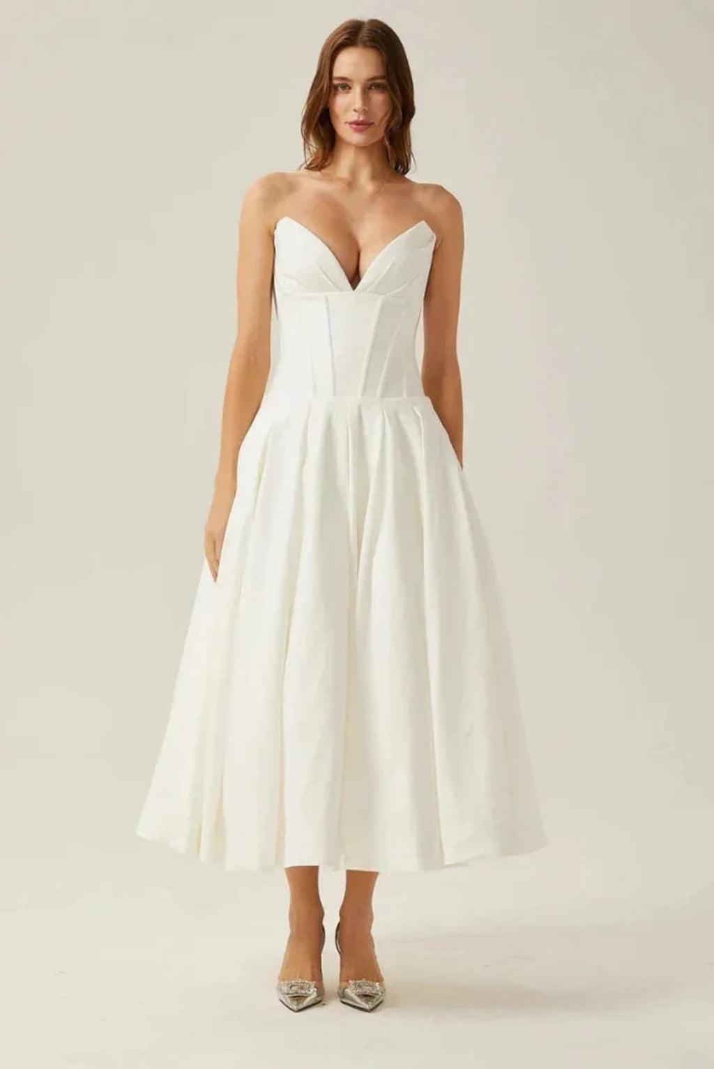 Woman modeling a strapless tea-length dress with pleated skirt.
