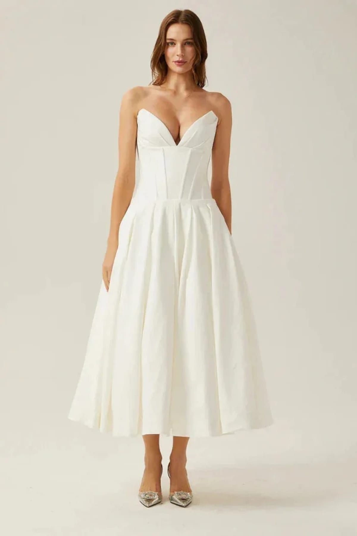 Woman modeling a strapless tea-length dress with pleated skirt.