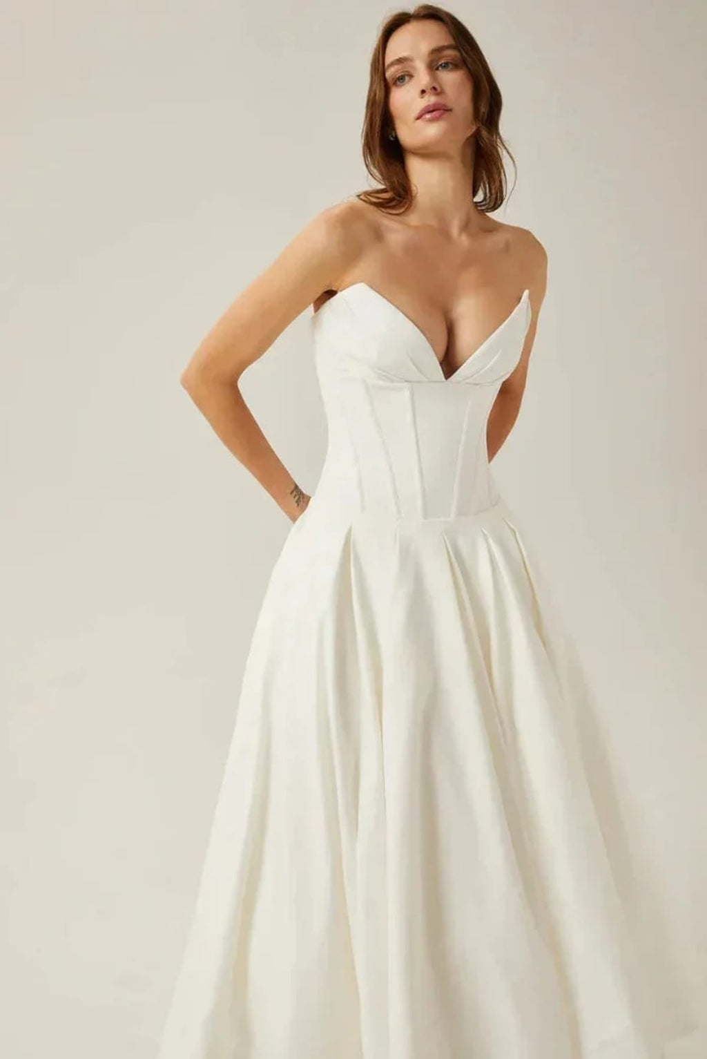 Woman modeling a strapless tea-length dress with pleated skirt.