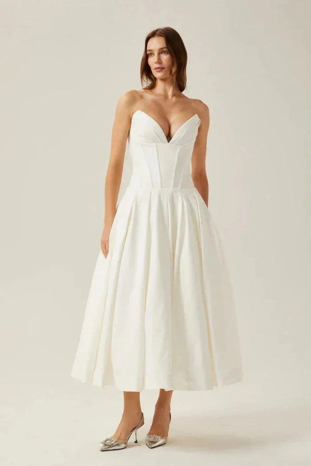 Woman modeling a strapless tea-length dress with pleated skirt.