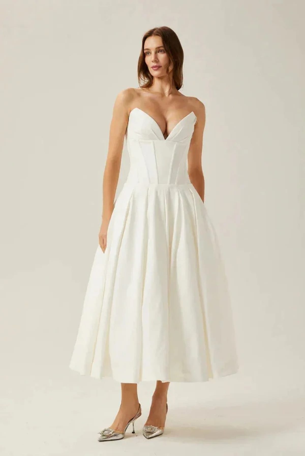 Woman modeling a strapless tea-length dress with pleated skirt.