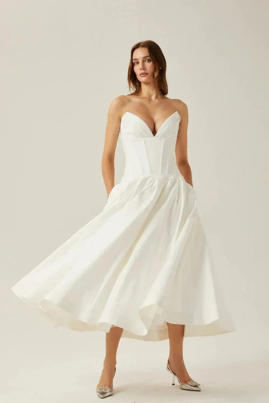 Woman modeling a strapless tea-length dress with pleated skirt.