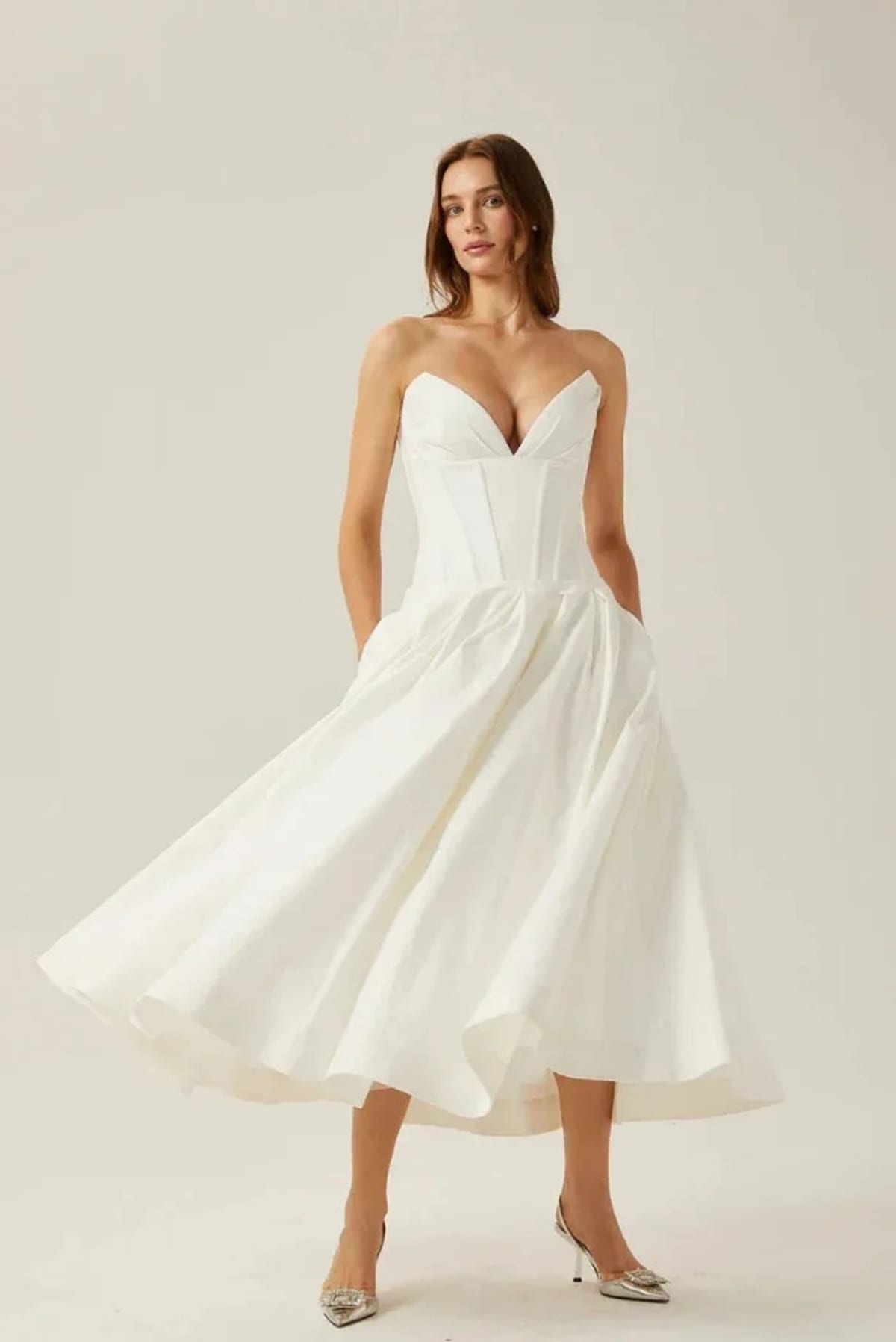 Woman modeling a strapless tea-length dress with pleated skirt.