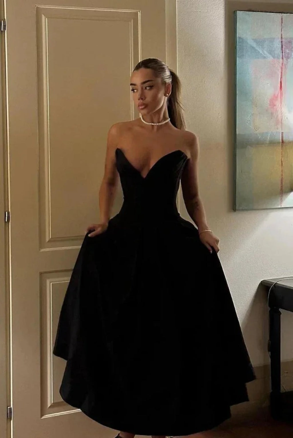 Woman modeling a strapless tea-length dress with pleated skirt.