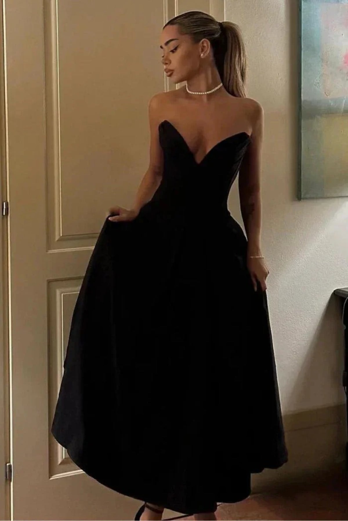 Woman modeling a strapless tea-length dress with pleated skirt.