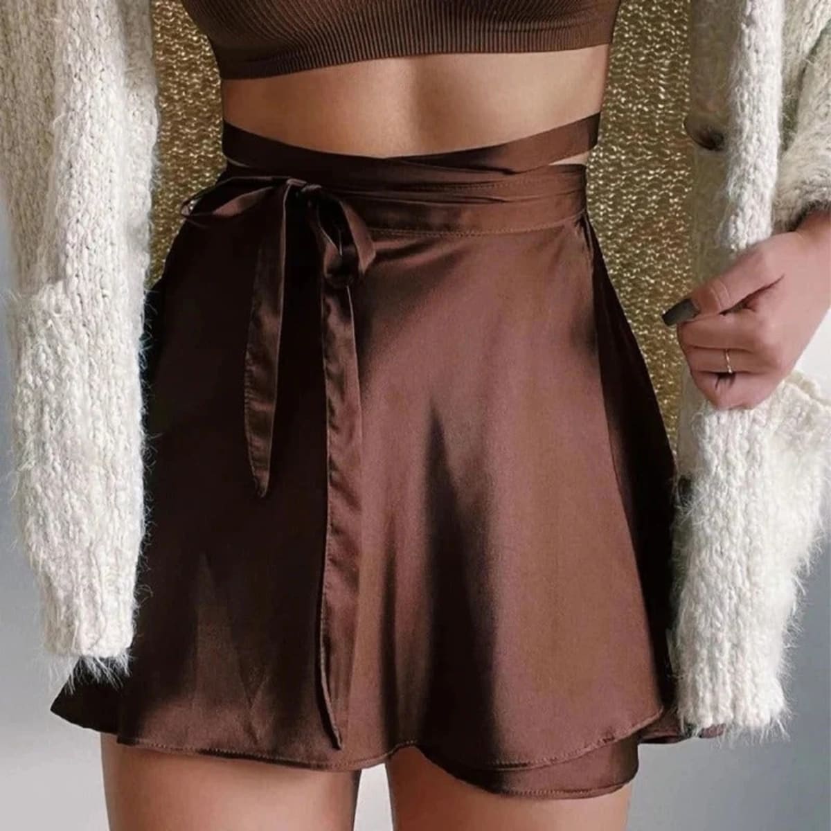 Model wearing a black satin wrap mini skirt with tie waist.