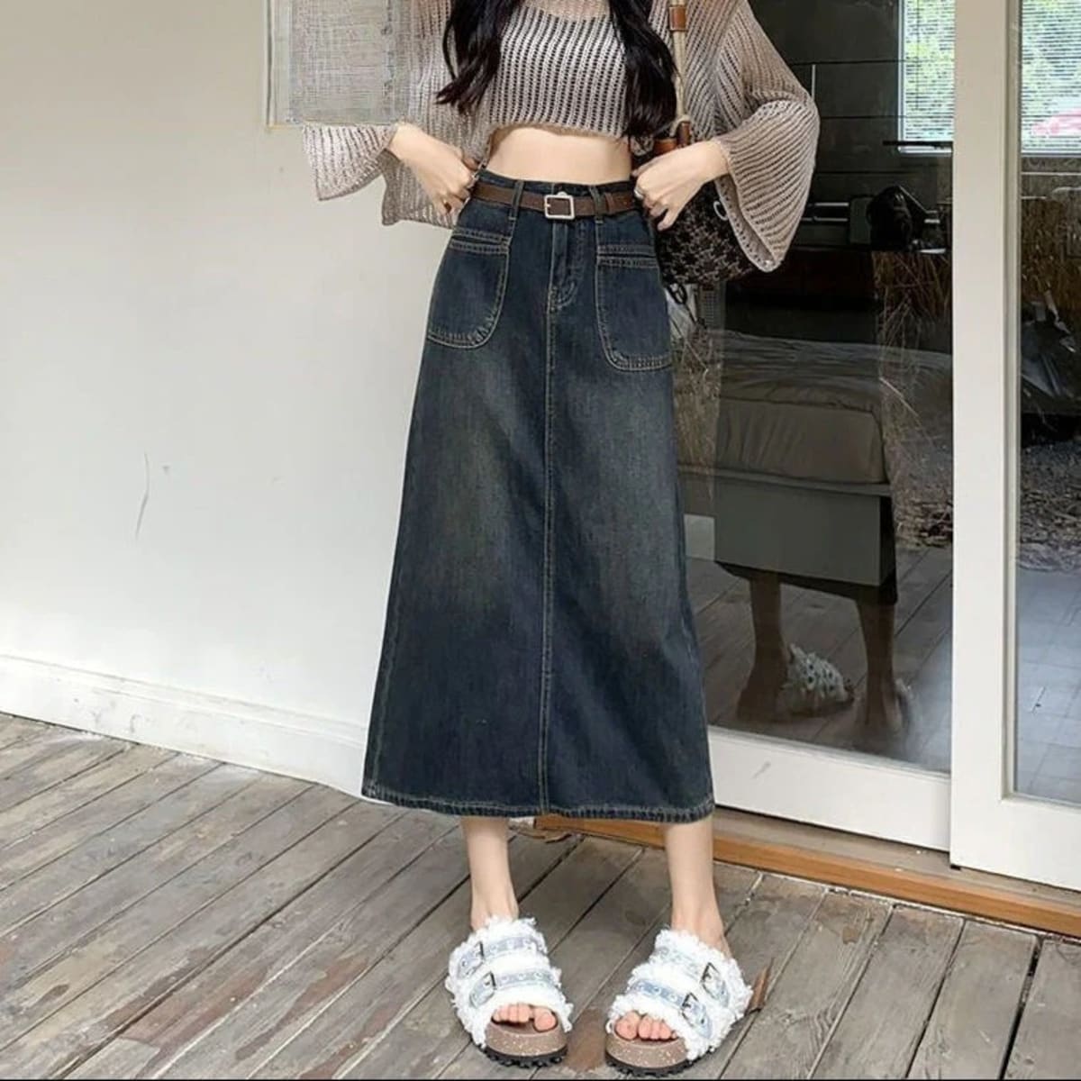 Woman wearing A-line midi denim skirt with front pockets and belt.