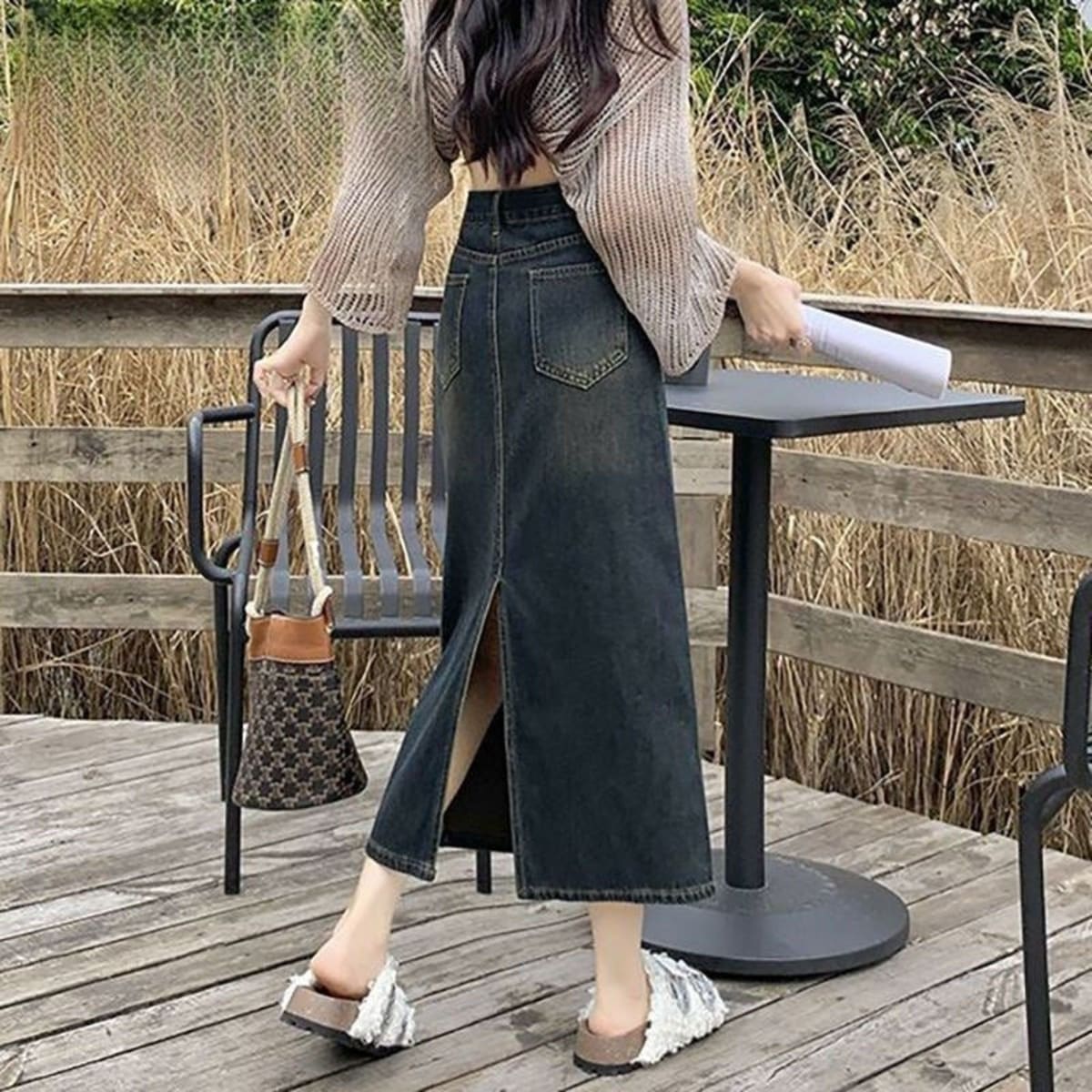 Woman wearing A-line midi denim skirt with front pockets and belt.