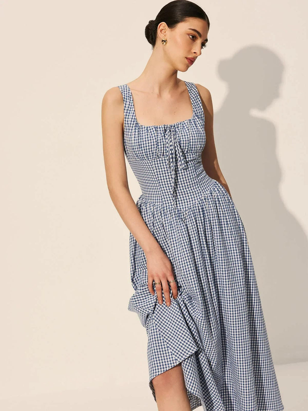 Woman wearing a gingham midi dress with square neck and smocked bodice.
