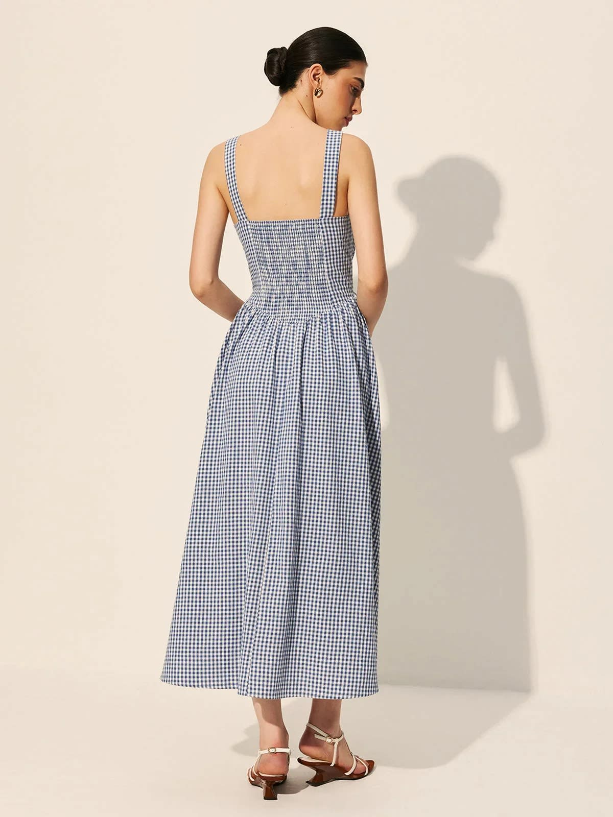 Woman wearing a gingham midi dress with square neck and smocked bodice.