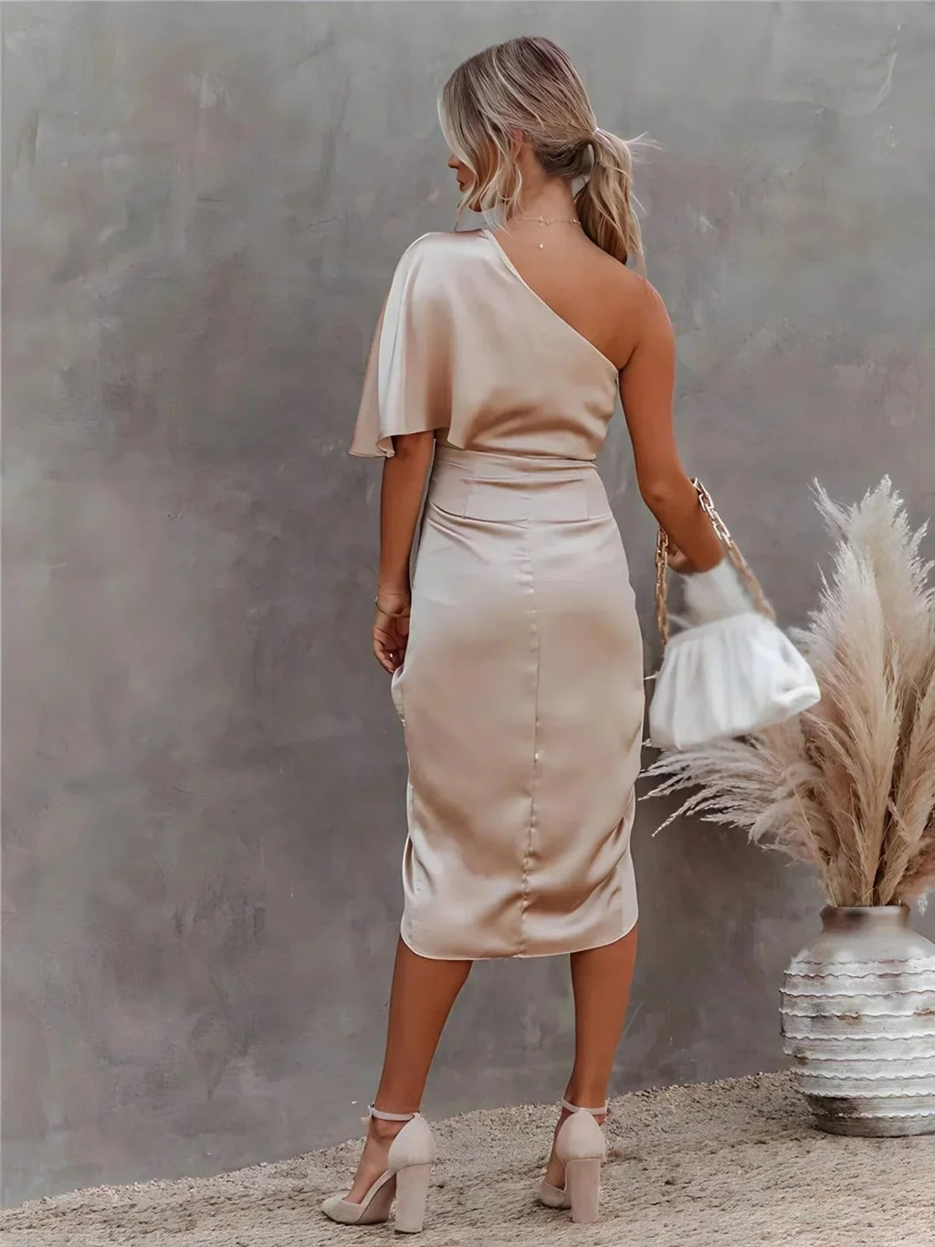 Woman in a one-shoulder black midi dress with draped bodice and ruched wrap skirt.