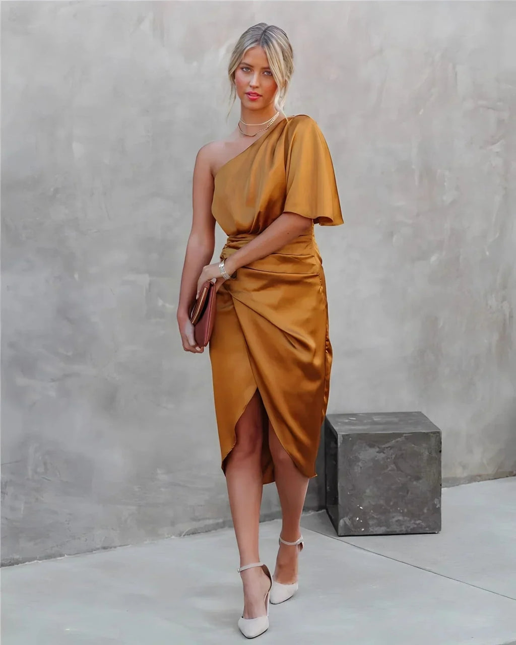 Woman in a one-shoulder black midi dress with draped bodice and ruched wrap skirt.
