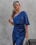 Woman in a one-shoulder black midi dress with draped bodice and ruched wrap skirt.