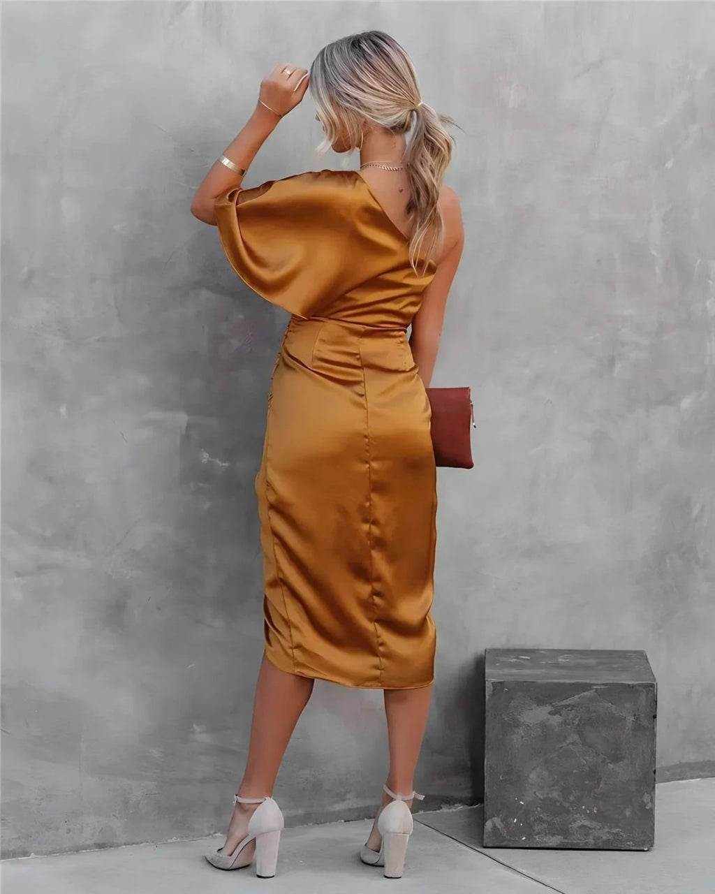 Woman in a one-shoulder black midi dress with draped bodice and ruched wrap skirt.