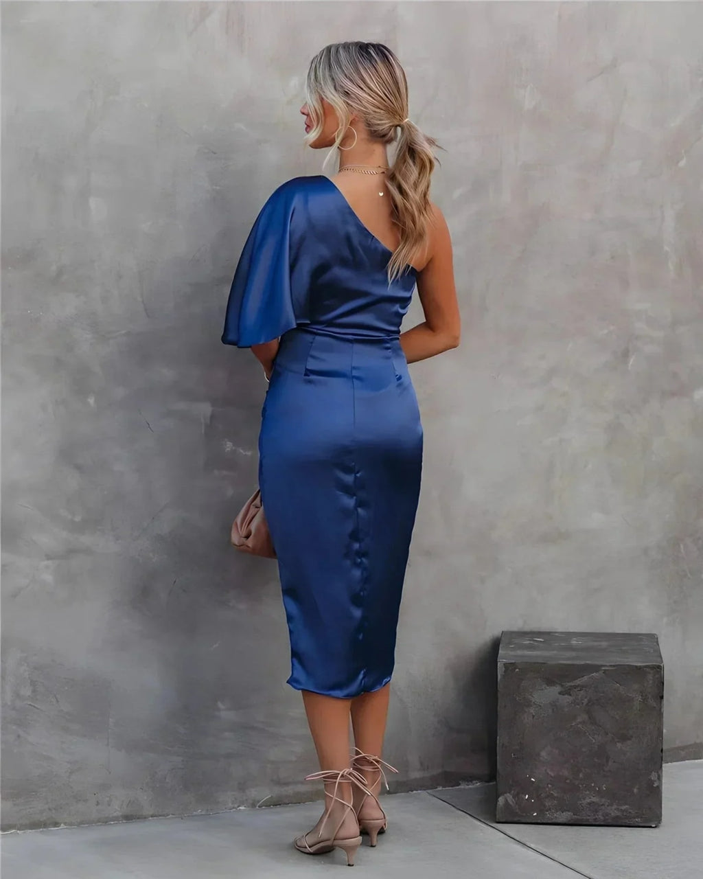 Woman in a one-shoulder black midi dress with draped bodice and ruched wrap skirt.