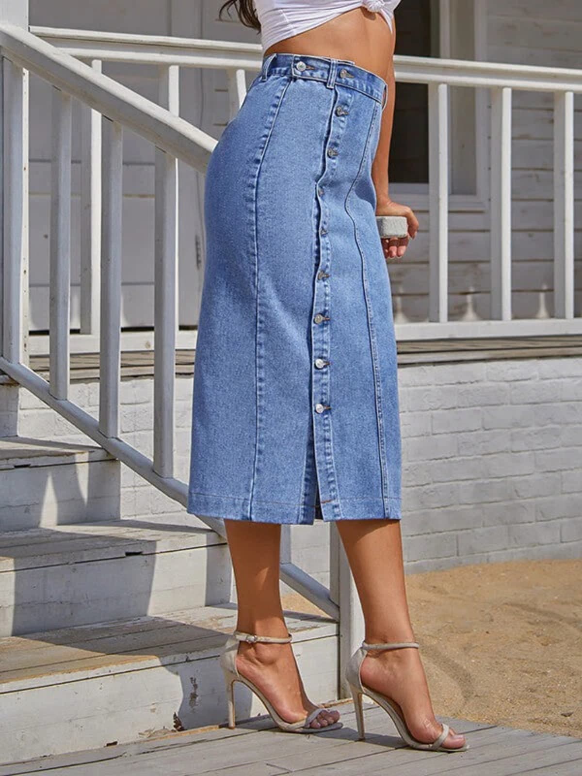 Woman wearing a high-waisted denim midi skirt with a button-front and side slit outdoors.