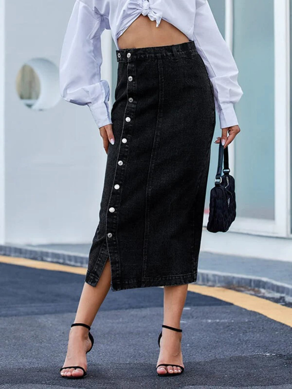Woman wearing a high-waisted denim midi skirt with a button-front and side slit outdoors.