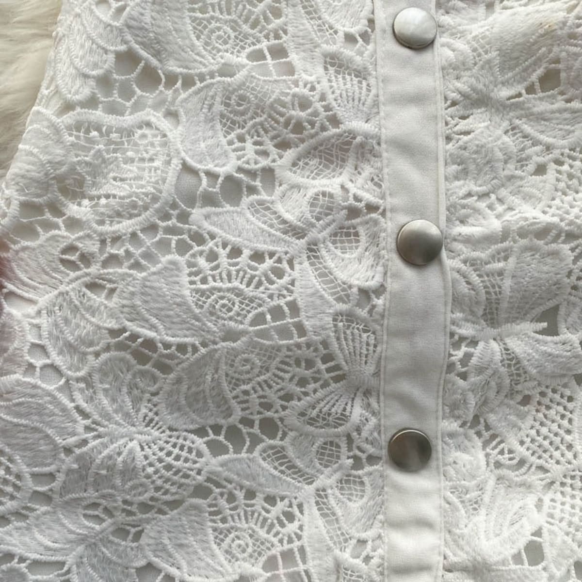 Sleeveless white lace midi dress with embellished skirt and button-down front.