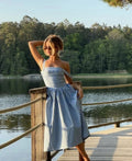 Woman wearing a gingham strapless midi dress on a dock by a lake.