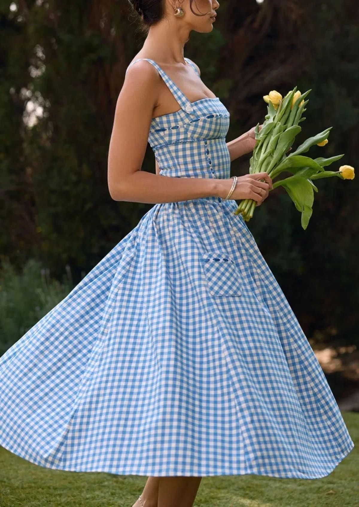 Woman wearing a gingham strapless midi dress on a dock by a lake.