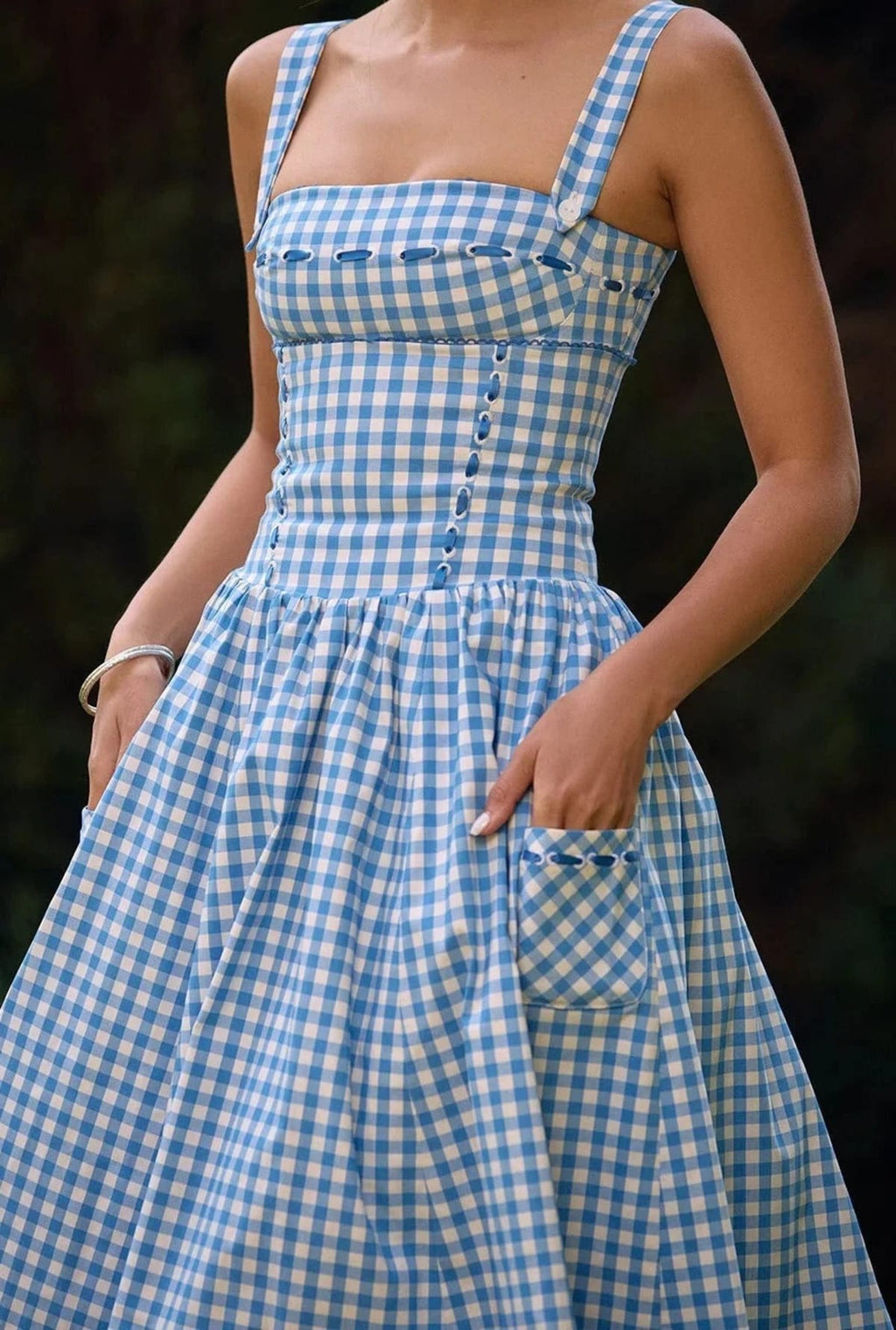 Woman wearing a gingham strapless midi dress on a dock by a lake.