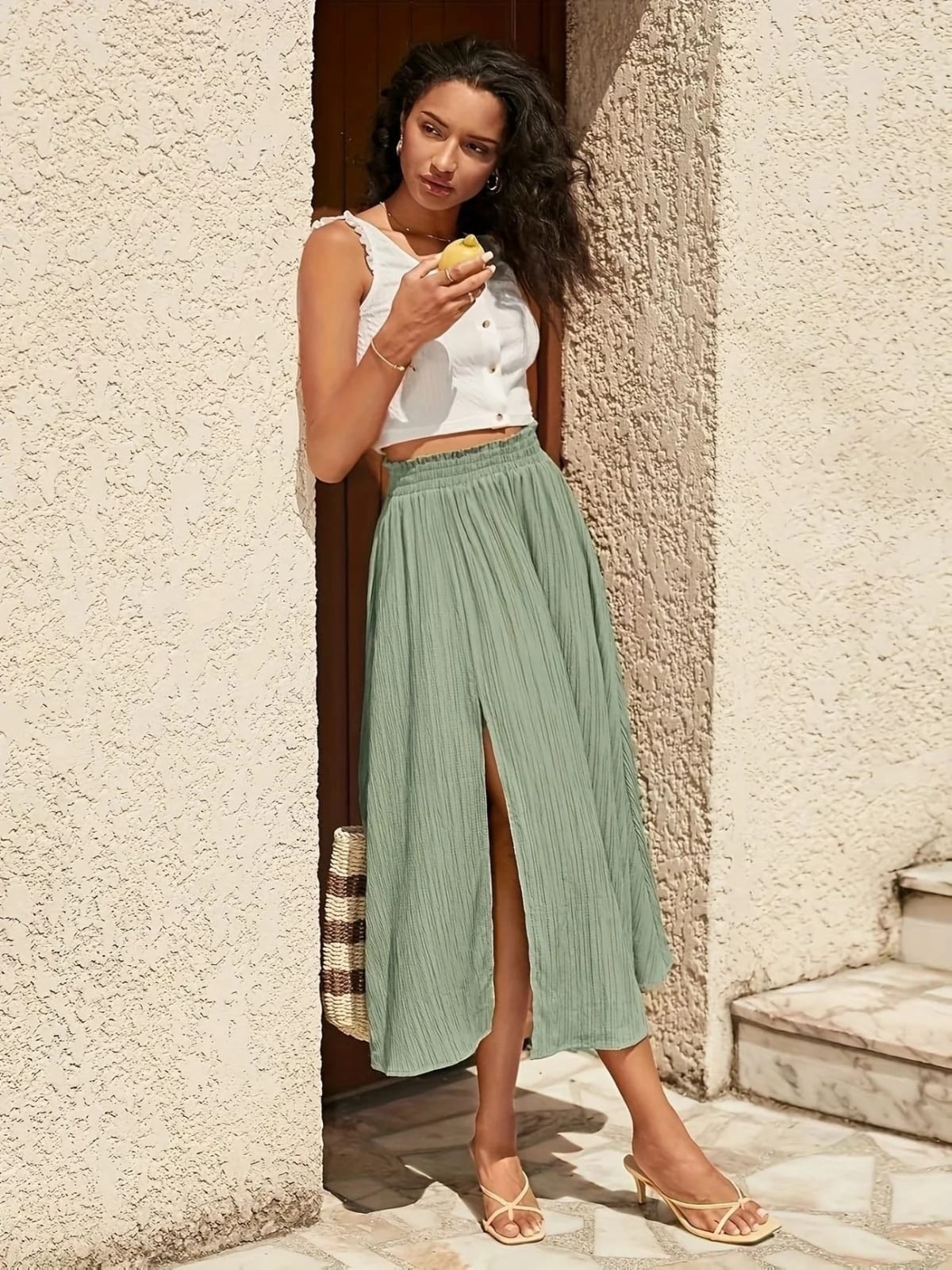 Woman wearing a midi skirt with smocked waist and front slit.